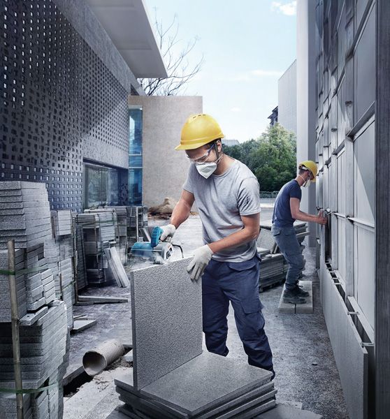 A person wearing safety equipment cuts a concrete panel with a power saw outdoors.