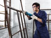 Person wearing safety equipment uses a straight grinder on a metal window frame.