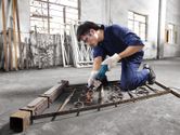 A person wearing safety equipment grinds metal on a gate frame, creating sparks.