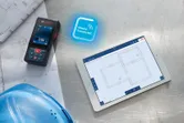 Laser measure beside blueprints and a hard hat, with a tablet displaying floor plans.