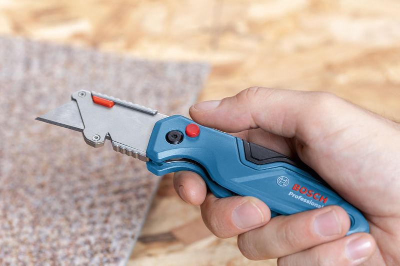 Person holds a utility knife, preparing to cut a piece of carpet.