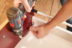 Person installing a flexible metal hose on furniture using a power drill.