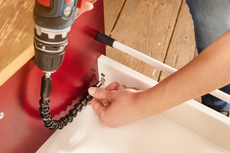 Person using a power drill with a flexible attachment to assemble furniture.