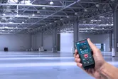 A person uses a laser measure in a large, empty industrial warehouse.