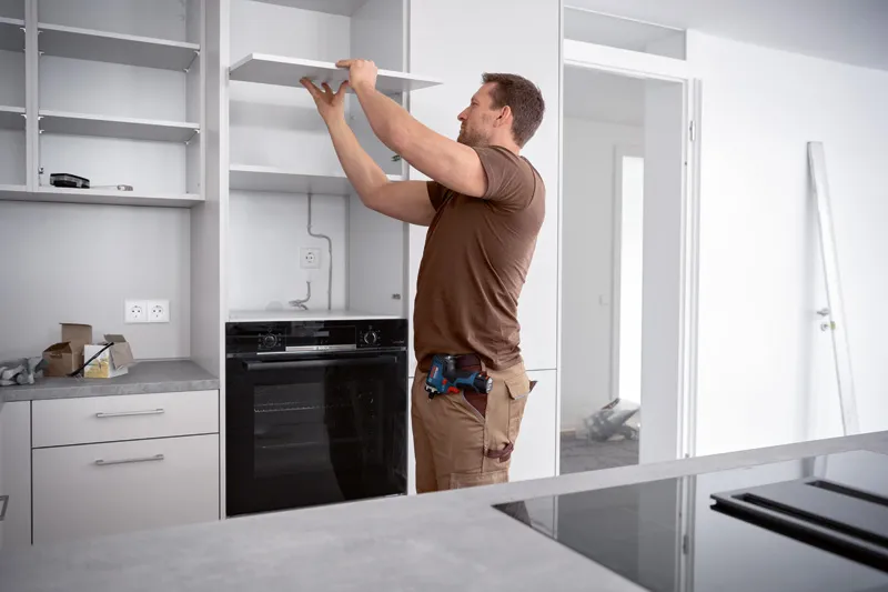 A person installs a kitchen shelf using a cordless screwdriver.