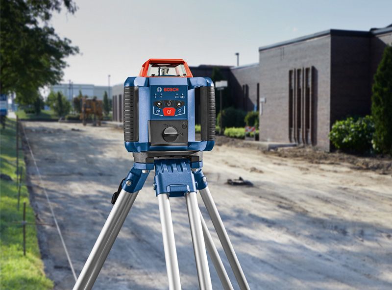 Laser leveling tool set on a tripod at a construction site beside a building.