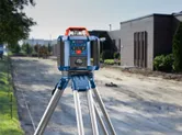 Laser leveling tool set on a tripod at a construction site beside a building.