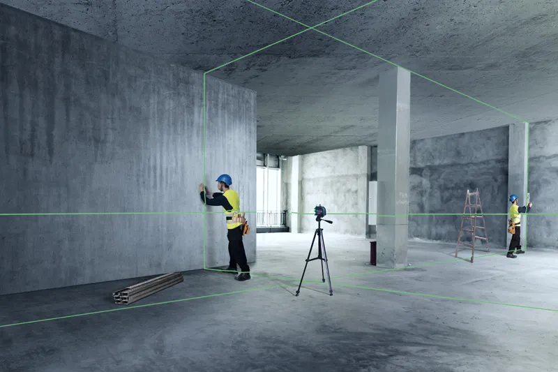 Two workers wearing safety equipment align interior walls using a laser leveling tool.