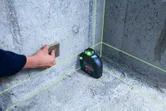 Person using a sanding block on a concrete wall, next to an active laser leveling tool.