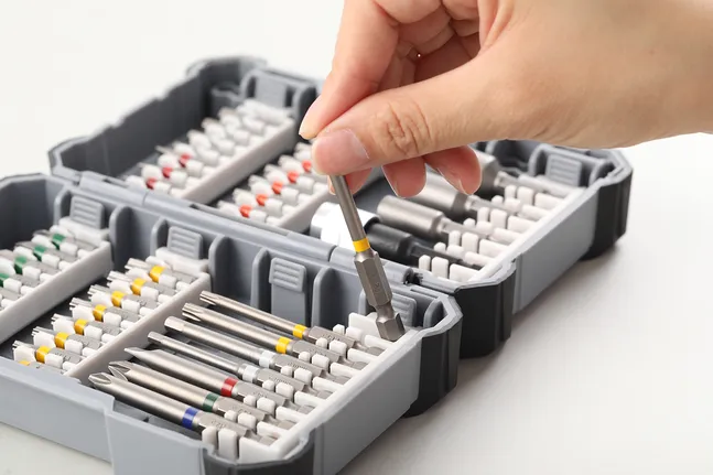 Person picking a screwdriver bit from a case containing assorted bits and accessories.