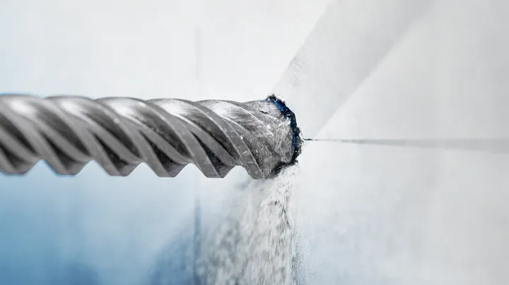 Drill bit boring into a concrete wall, creating dust.