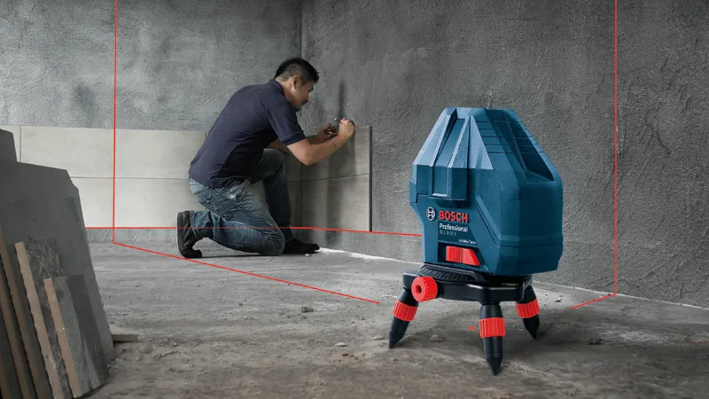 A person aligns tiles on a wall using a laser leveling tool.