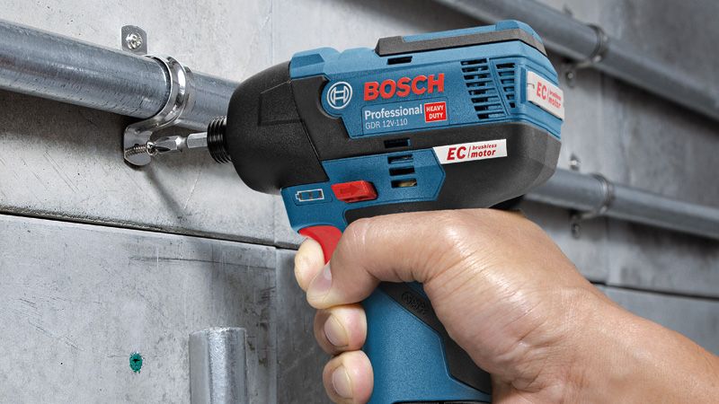 A person uses a cordless impact driver to fasten a screw into a metal conduit.