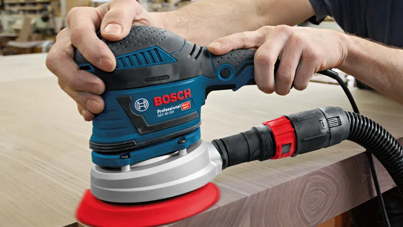 A person uses a random orbit sander to smooth the edge of a wooden surface.