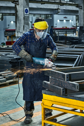 Person wearing safety equipment grinds a metal beam with sparks flying.