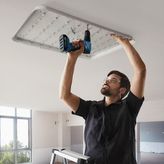A person wearing safety equipment installs a large ceiling light using a cordless drill.