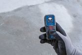 Person wearing safety equipment holds a laser measure over a concrete surface.