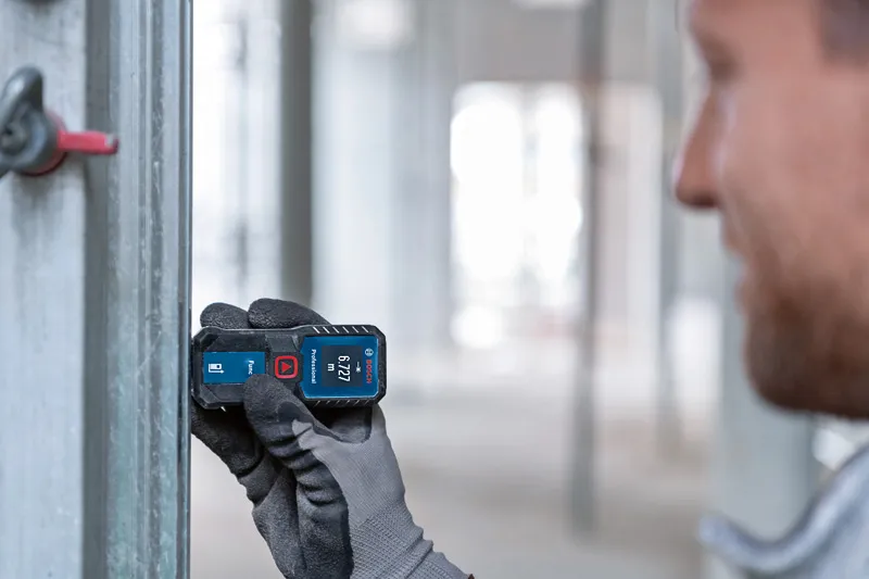 Person wearing safety equipment uses a laser measure against a metal beam.