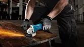A person wearing safety equipment grinds a metal beam with an angle grinder, producing sparks.