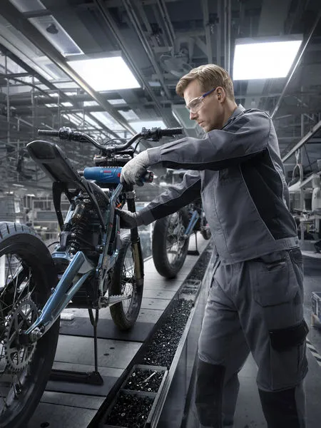 A person wearing safety equipment assembles a motorcycle frame in a factory.