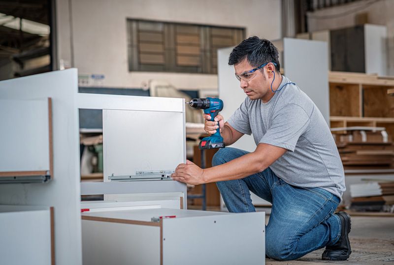 Person wearing safety equipment assembles furniture using a cordless drill.