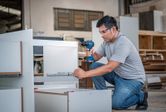 Person wearing safety equipment assembles furniture using a cordless drill.