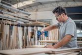 A person wearing safety equipment drills into wood in a workshop.