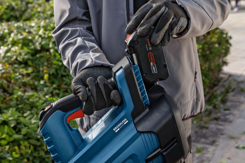 A person wearing safety equipment inserts a battery into a cordless leaf blower outdoors.