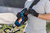 A person wearing safety equipment attaches a battery to a cordless grass trimmer.
