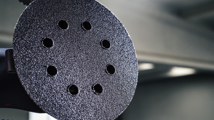 Close-up of a circular sanding pad with multiple holes against a blurred workshop background.