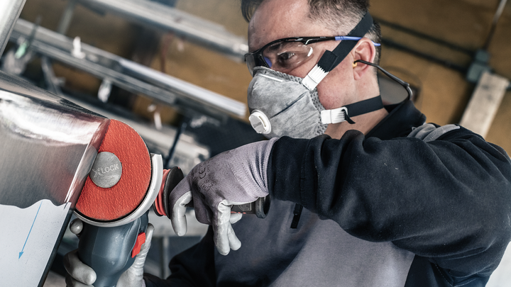 Person wearing safety equipment polishes metal with a power tool.