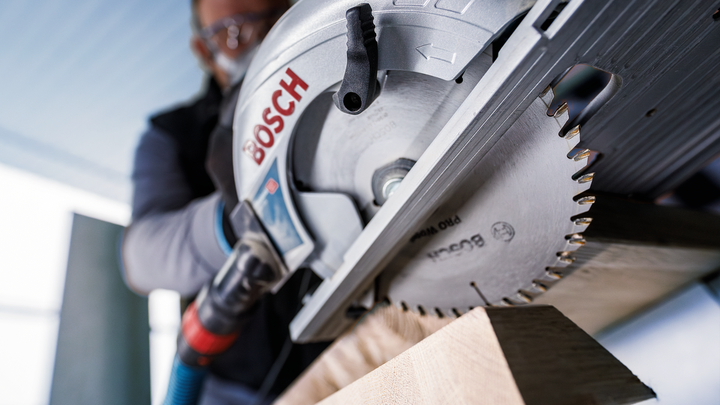 A person wearing safety equipment cuts wood with a circular saw.
