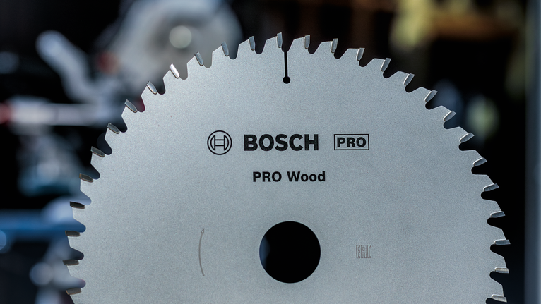 Circular saw blade with sharp teeth shown in a workshop setting.