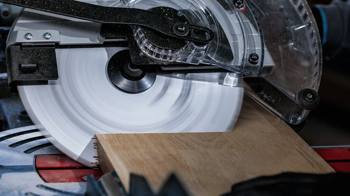 Person wearing safety equipment cuts a wooden board with a circular saw.