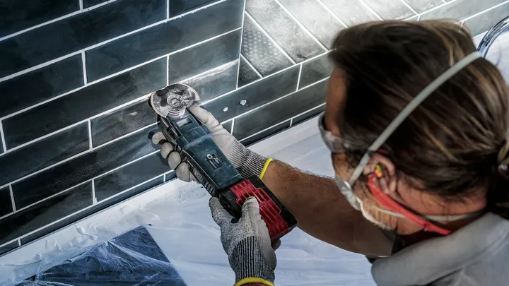 Person wearing safety equipment uses an angle grinder to cut black wall tiles.