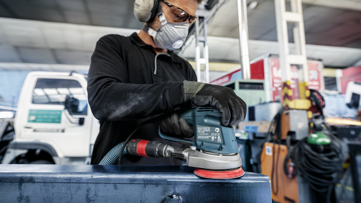 Person wearing safety equipment uses a power sander on a metal surface.