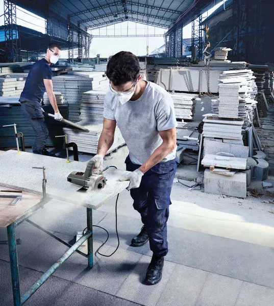 Person wearing safety equipment uses a marble saw to cut a stone slab indoors.