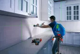 Person aligning kitchen cabinets with a laser leveling tool on a tripod.