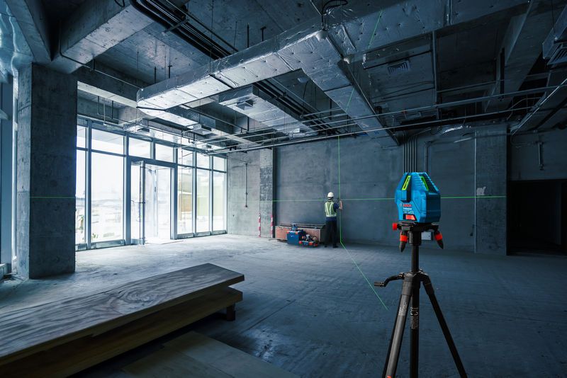 A person wearing safety equipment aligns walls using a laser leveling tool in a construction site.