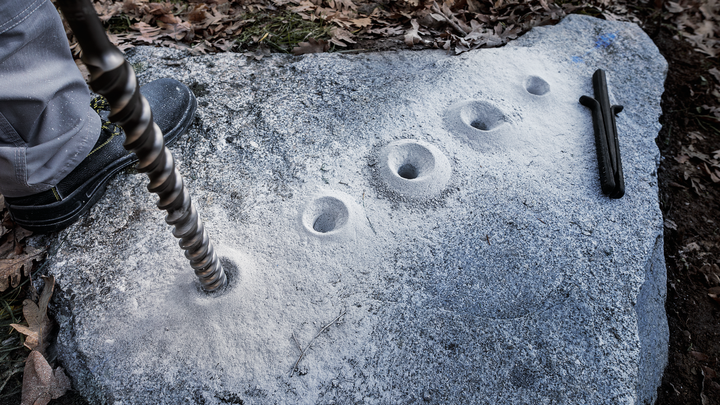 Person drilling multiple holes into a large stone outdoors.