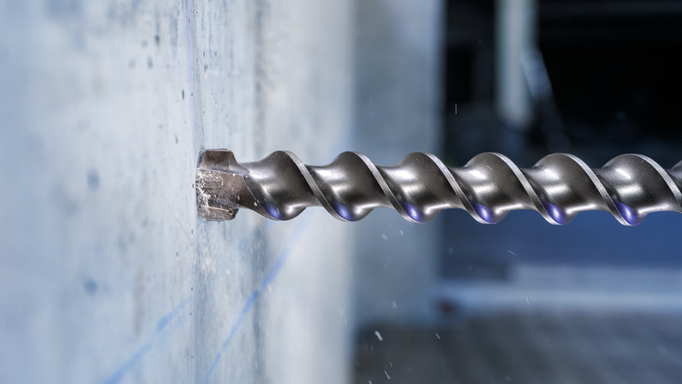 Large auger drill bit boring into a concrete wall.