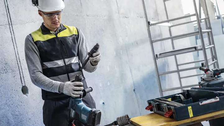 A person wearing safety equipment prepares a power tool on a worksite.