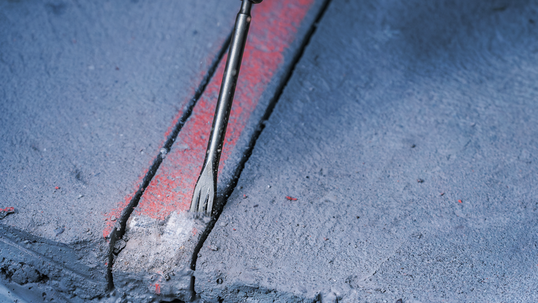 Chisel breaking a groove into a marked concrete surface.