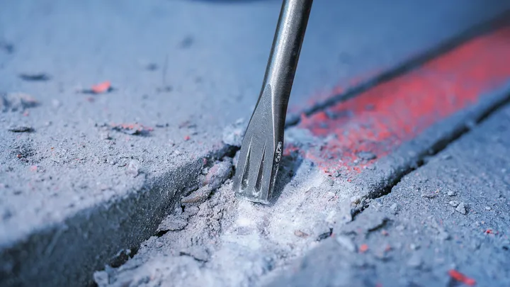 Chisel bit breaking concrete along a marked line.