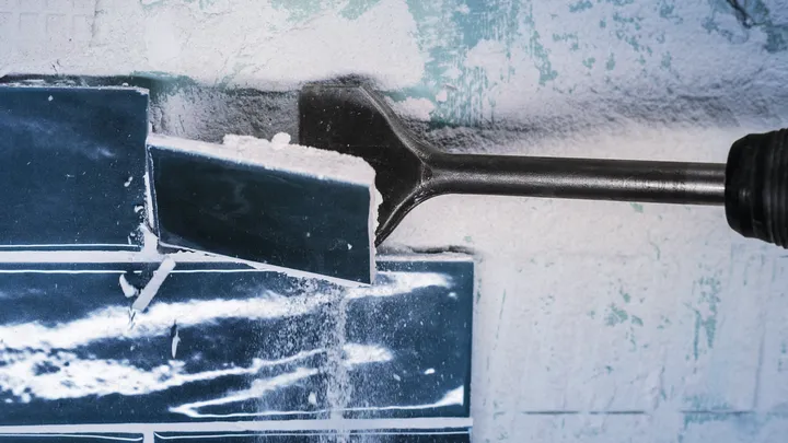 Chisel attachment removes a ceramic tile from a wall.