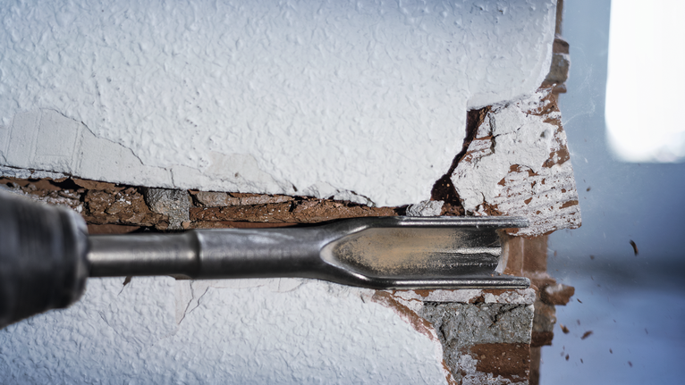 Demolition chisel breaking through plaster and brick wall.