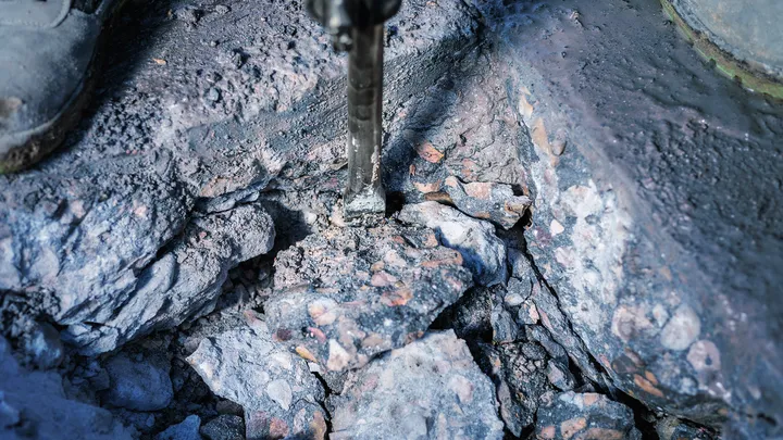 Demolition hammer breaking concrete into large rubble pieces.