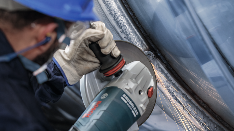 A person wearing safety equipment grinds metal, producing sparks.