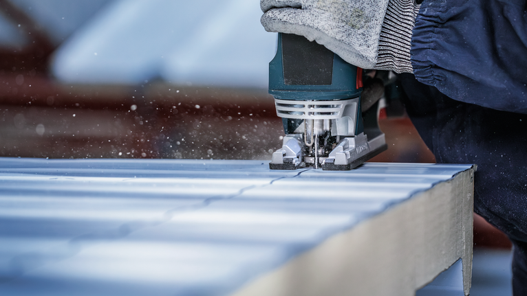 Person wearing safety equipment uses a jigsaw to cut a straight line in a panel.