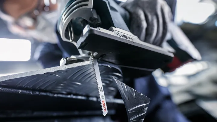 A person wearing safety equipment cuts patterned metal with a jigsaw.